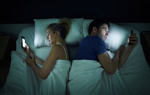 image of two people laying in bed on their phones